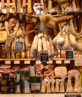 Salumeria italiana con salumi appesi, formaggi, olio d’oliva e cartello 'Peace Love n Bruschetta'