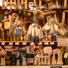 Mercado italiano de delicatessen con embutidos colgados, quesos, aceite de oliva y cartel de 'Peace Love n Bruschetta'