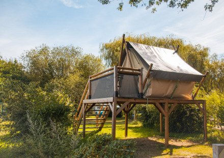 Safari tent op een houten platform in een groene, natuurlijke omgeving, gefotografeerd overdag.