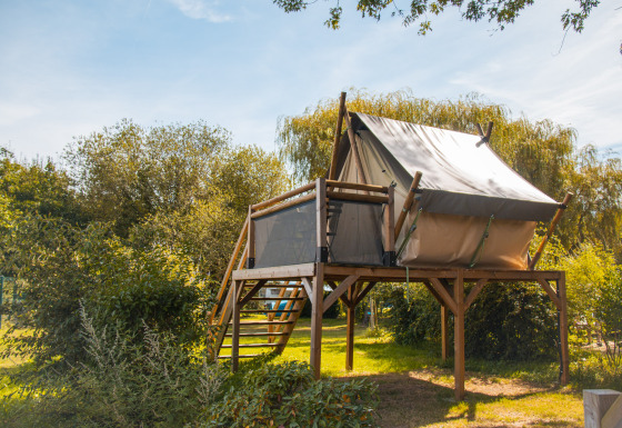 Safari tent op een houten platform te midden van groen en natuur, gefotografeerd bij daglicht.