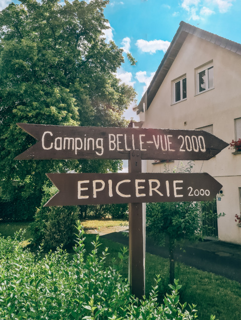 Wooden signposts at Camping Belle-Vue 2000 in Echternach, Luxembourg, pointing to campsite and grocery store.
