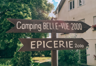 Wooden signposts at Camping Belle-Vue 2000 in Echternach, Luxembourg, pointing to campsite and grocery store.
