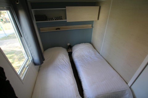 Dos camas individuales con sábanas blancas en una pequeña habitación en Mobilhome Loggia, Camping Belle-Vue 2000, Luxemburgo.