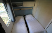 Dos camas individuales con sábanas blancas en una pequeña habitación en Mobilhome Loggia, Camping Belle-Vue 2000, Luxemburgo.