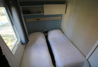 Dos camas individuales con sábanas blancas en una pequeña habitación en Mobilhome Loggia, Camping Belle-Vue 2000, Luxemburgo.