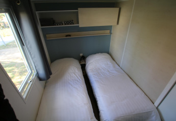 Dos camas individuales con sábanas blancas en una pequeña habitación en Mobilhome Loggia, Camping Belle-Vue 2000, Luxemburgo.
