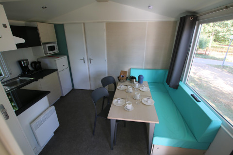 Intérieur du Mobilhome Loggia au Camping Belle-Vue 2000 avec cuisine, table et banquette turquoise.