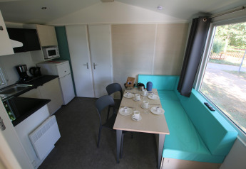 Interior of Mobilhome Loggia at Camping Belle-Vue 2000 showing kitchen, table, and turquoise seating.