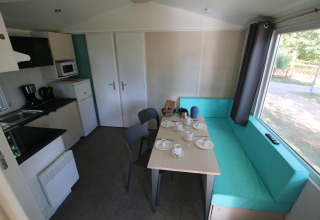 Interno della Mobilhome Loggia al Camping Belle-Vue 2000 con cucina, tavolo e seduta turchese.