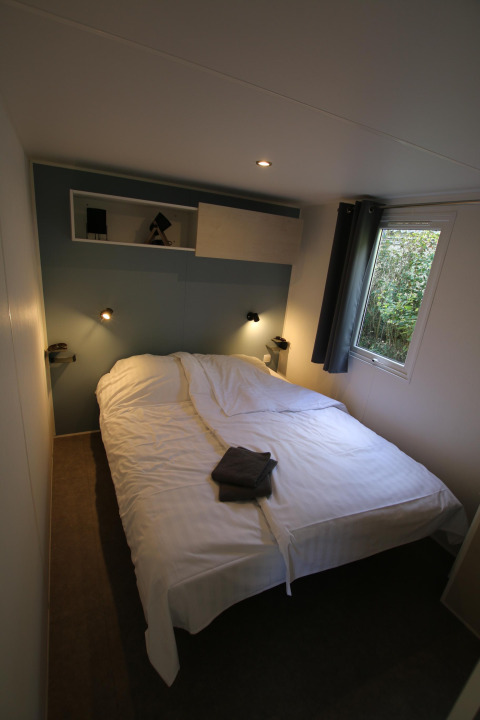 Chambre du Mobilhome Loggia au Camping Belle-Vue 2000 au Luxembourg, avec lit double et fenêtre lumineuse.
