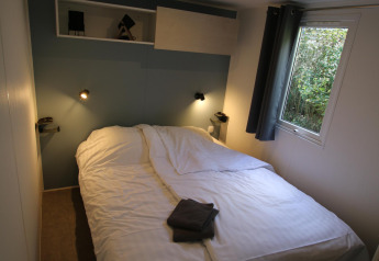 Chambre du Mobilhome Loggia au Camping Belle-Vue 2000 au Luxembourg, avec lit double et fenêtre lumineuse.
