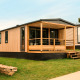 Modern Mobilhome O'Hara Living chalet met houten gevel en overdekte veranda op een grasveld.