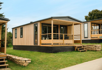 Modernes Mobilhome O'Hara Living Chalet mit Holzverkleidung und überdachter Terrasse auf Rasenfläche.