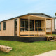 Et moderne Mobilhome O'Hara Living chalet med træfacade og overdækket terrasse på græsset område.