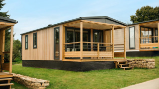 Modernes Mobilhome O'Hara Living Chalet mit Holzverkleidung und überdachter Terrasse auf Rasenfläche.