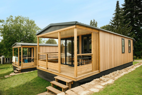 Chalet moderne en bois Mobilhome O'Hara Living au Camping Belle-Vue 2000 au Luxembourg entouré de verdure.