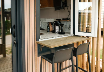 Outdoor-Sitzbereich mit zwei Barstühlen am Fenster, fotografiert im Mobilhome O'Hara Living, Camping Belle-Vue 2000.