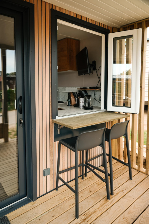 Zona pranzo all'aperto con due sgabelli al bancone finestra presso Mobilhome O'Hara Living, Camping Belle-Vue 2000.