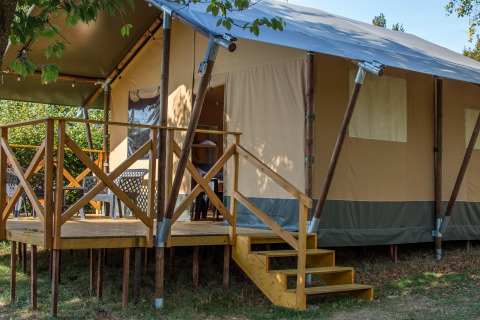 Vista de la Safari tent XL con terraza elevada de madera, escaleras y asientos al aire libre rodeados de naturaleza.