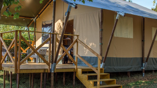Safari tent XL mit erhöhter Holzterrasse, Treppe und Sitzbereichen im Freien in grüner Umgebung.