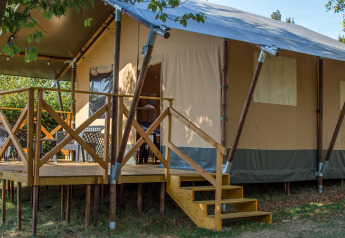 Safari tent XL mit erhöhter Holzterrasse, Treppe und Sitzbereichen im Freien in grüner Umgebung.