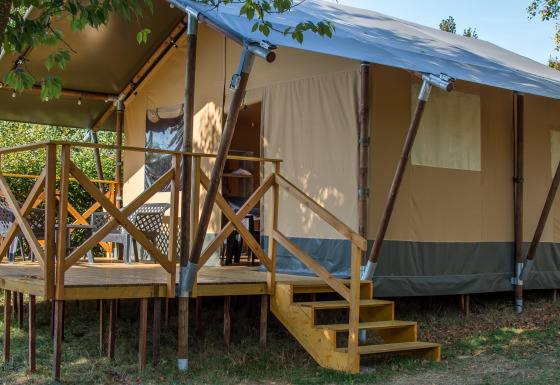 Vista de la Safari tent XL con terraza elevada de madera, escaleras y asientos al aire libre rodeados de naturaleza.