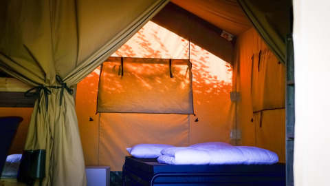 Interior de una tienda Safari XL en Camping Belle-Vue 2000, Luxemburgo, con cama cómoda y luz cálida.