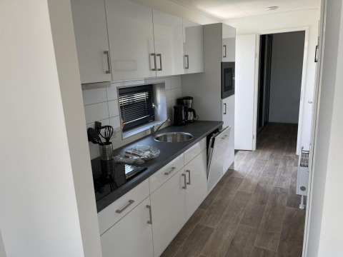 Cocina moderna en alojamiento glamping con gabinetes blancos, encimera negra y cafetera sobre la mesa.