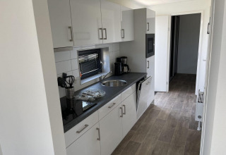 Cocina moderna en alojamiento glamping con gabinetes blancos, encimera negra y cafetera sobre la mesa.