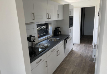 Cucina moderna in una sistemazione glamping con mobili bianchi, piano nero e macchina del caffè.