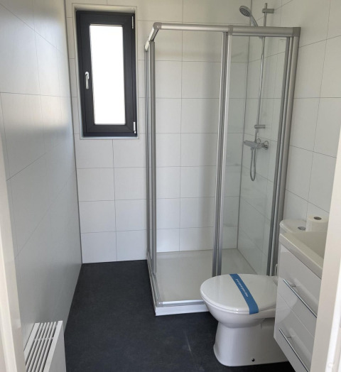 Bagno moderno per glamping con cabina doccia, wc e piccolo lavandino, pareti bianche, pavimento scuro.