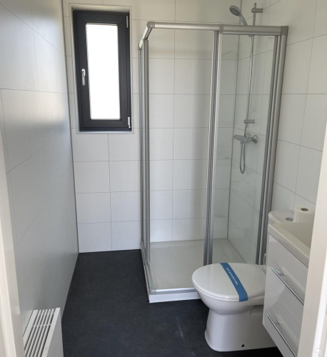 Modernes Glamping-Badezimmer mit Duschkabine, Toilette und kleinem Waschbecken, hell gefliest.