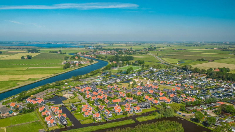 Aerial view of a glamping accommodation with red-roofed cabins, canals, and green fields on a sunny day.