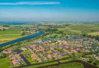Vista aérea de un alojamiento glamping con cabañas de tejados rojos, canales y verdes campos alrededor.