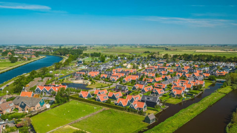 Luchtfoto van een glampingresort met huisjes met rode daken, omringd door water en weilanden.