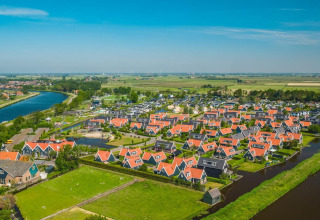 Luchtfoto van een glampingverblijf met rode daken, omgeven door waterlopen en groene velden.