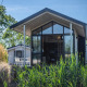 Moderne Tiny House-lodge med store vinduer, udendørs siddeplads og omkringliggende naturgrønne omgivelser.