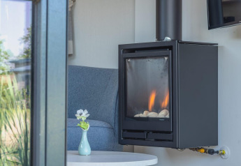 Moderne brændeovn og hyggelig stol i et Tiny House ved De Rijp, Holland, set gennem et vindue.