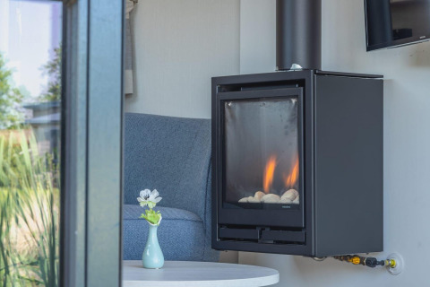Modern wood stove and cozy chair in a Tiny House at De Rijp, Netherlands, viewed through a window.