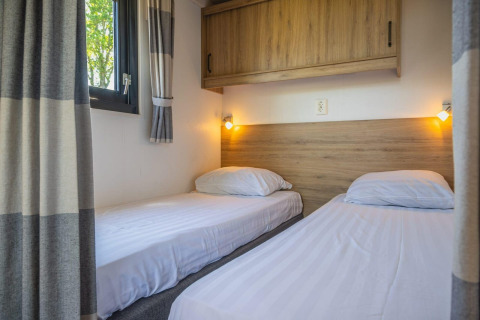 Deux lits simples avec draps blancs dans Tiny House à De Rijp, Pays-Bas, meubles bois et fenêtre.