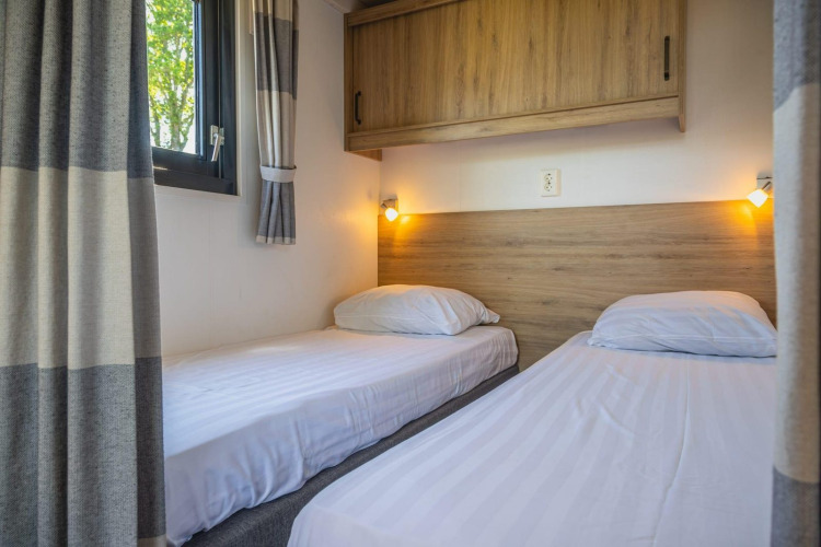 Dos camas individuales con ropa de cama blanca en Tiny House en De Rijp, Países Bajos, armarios de madera.