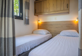 Twee eenpersoonsbedden met wit linnengoed in Tiny House bij De Rijp, Nederland, houten kast en raam.