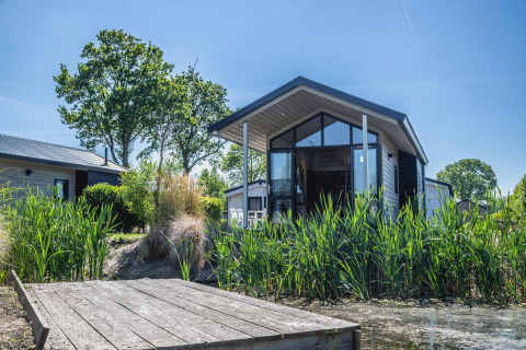 Moderne tiny house lodge aan het water in De Rijp, Nederland, omgeven door groen en blauwe lucht.