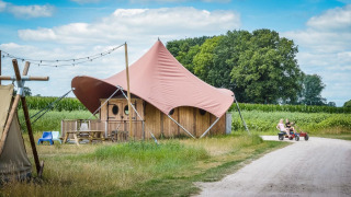Tenda safari Dream suite a Holiday Park Mölke nei Paesi Bassi con bambini che guidano un go-kart fuori.