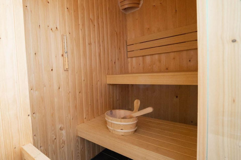 Interieur van een houten sauna met bank en emmer in een gezellige glamping accommodatie voor ontspanning.
