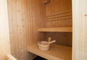 Vista interna di una sauna in legno con panche e secchio in un alloggio glamping accogliente.
