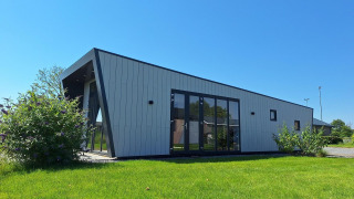 Moderne lodge genaamd Just Nature in De Rijp, Nederland, omringd door gras en een blauwe lucht.