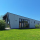 En moderne lodge ved navn Just Nature på De Rijp i Holland, omgivet af grønt græs og blå himmel.