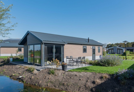 Moderne Velthorst lodge met glazen gevel, buitenterras, tuinset en groen gazon aan het water.