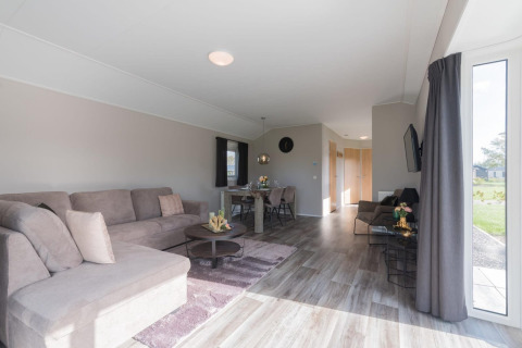 Helles, modernes Wohnzimmer einer Velthorst-Lodge in De Rijp, Niederlande, mit Sofa, Esstisch und großen Fenstern.